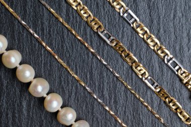 Taş bir tahtanın üzerinde farklı altın zincirler ve inciler. Kapat..