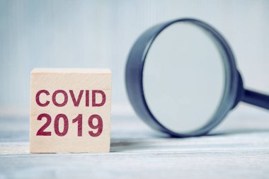 Üzerinde yazıt virüsü olan tahta bloklar, büyüteç yanında COVID-19. Kapat..