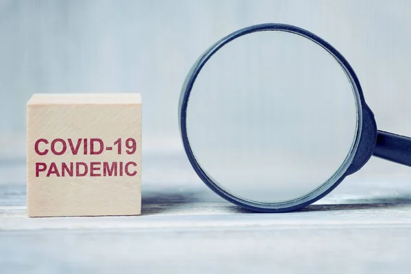 Wooden blocks with the inscription virus - COVID-19 PANDEMIC next to a magnifying glass. Close up.