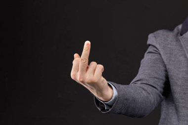 A man in a jacket shows a fuck you with his hand on a black background. Close up.