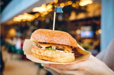 Kız restoranın arka planında bir hamburger tutuyor. Kapat..