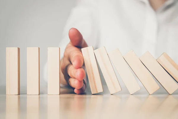 The concept of protection against the collapse of stock markets - abstractly a hand on a table overlaps falling wooden blocks. Close up.