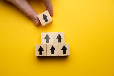 Başarılı bir iş konsepti. El, sarı arka planda okla ahşap bloğu tutuyor. Kapat..