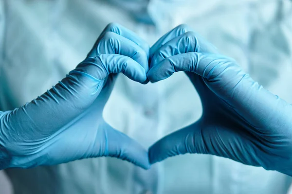 A doctor in blue medical gloves makes a heart out of his hands. Close up.