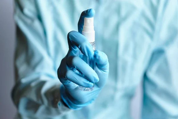 A doctor in a dressing gown and medical gloves shows how to use an antiseptic sanitizer. Close up.