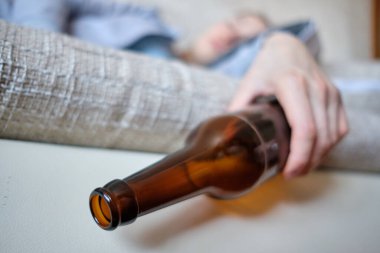 Kız kanepede uyuyor ve elinde bir şişe alkol tutuyor. Kapat..