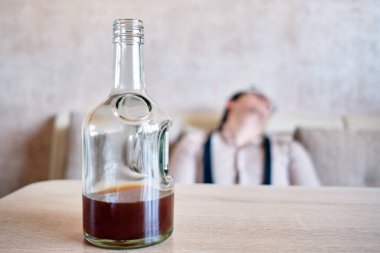 İşten sonra masada bir şişe alkolle kanepede uyuyan sarhoş bir adam. Kapat..