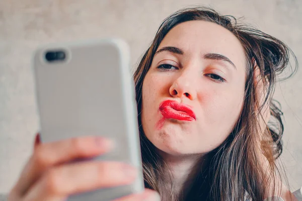 Drunk girl with smeared lipstick takes selfie pictures on the phone. Close up.