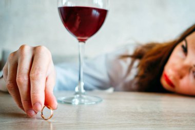 Kız ayrılık yüzünden üzgün ve bir bardak şarabın yanında alyans tutuyor. Kapat..