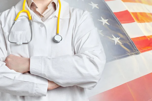 Male doctor in a coat with a stethoscope on the background of the American flag. Close up.