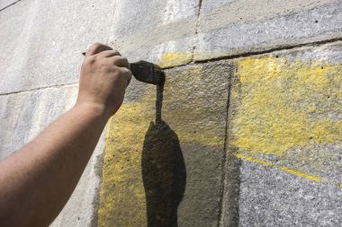 Elini duvar boyunca fırçalıyor. Kaba duvar kaplama.