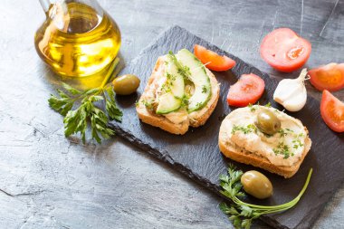 Siyah granit tahtada avokado ve mikro roka filizli humus sandviçleri.