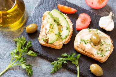 Siyah granit tahtada avokado ve mikro roka filizli humus sandviçleri.