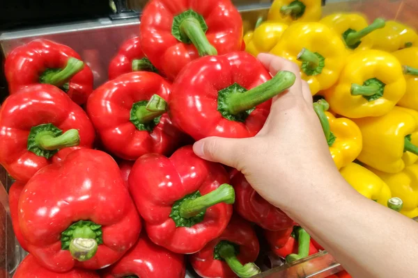 Dona de casa está comprando pimentas amarelas e vermelhas maduras em vegetais — Fotografia de Stock
