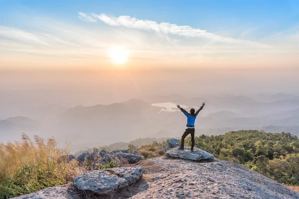 Homem bem sucedido escalada espalhando a mão no penhasco e desfrutar de vista do nascer do sol — Fotografia de Stock