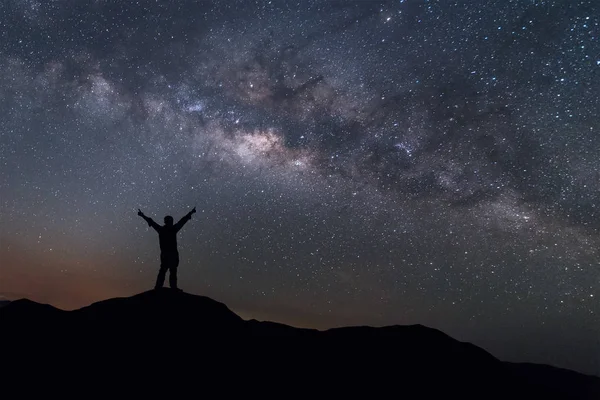 Samanyolu manzara. Mutlu adam gece gökyüzü ve arka plan üzerinde parlak yıldız ile dağın tepesinde duran silüeti. 