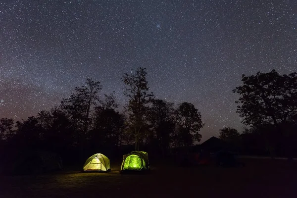 Camping tent glows under a night sky full of stars.