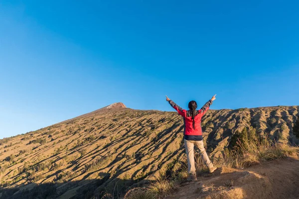 Женщина-турист носить красную куртку, распространяя руку, наслаждаться и счастливы с видом на вершину горы после завершения восхождения на гору Ринджани, Ломбок, Индонезия . — стоковое фото