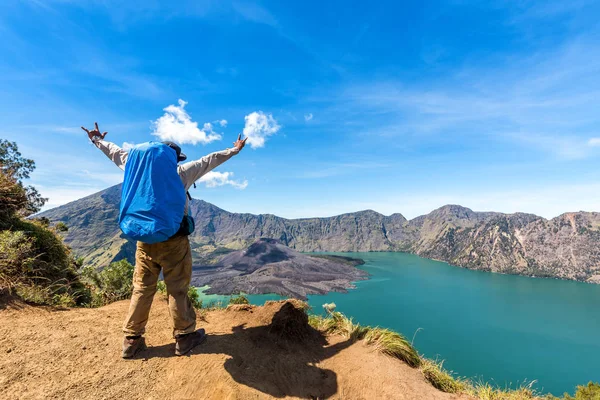 Турист с рюкзаком протягивая руку, наслаждайтесь активным вулканом Бару Яри, озером Сегара-Анак и вершиной горы Ринджани после завершения восхождения на гору Ринджани, Ломбок, Индонезия — стоковое фото