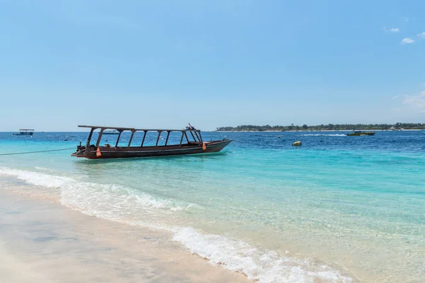 Małe drewniane łódź na niebieski plaża z pochmurnego nieba i wyspy Lombok na tle. Gili Trawangan, Indonezja. — Zdjęcie stockowe