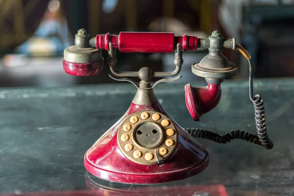 Old red telephone with rotary dial on glass table.