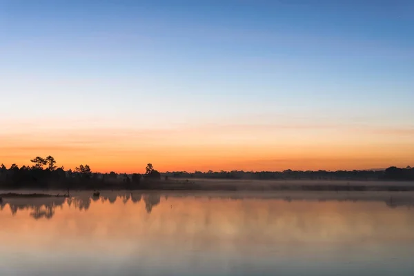 Morgensonnenaufgang über dem See mit Silhouettenbaum spiegelt sich auf der Wasseroberfläche bei phu kradueng, Nationalpark in Thailand. lizenzfreie Stockbilder