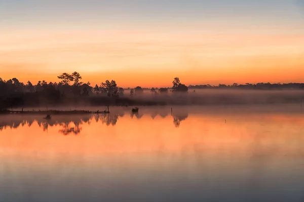 Manhã nascer do sol sobre o lago com árvore silhueta refletir sobre a superfície da água em Phu Kradaung, parque nacional na Tailândia . — Fotografia de Stock