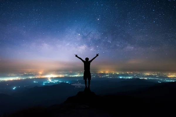 Silhouette of man spreading hand and enjoy to see the Milky Way above the light of countryside area and mountain. — Stock Photo, Image