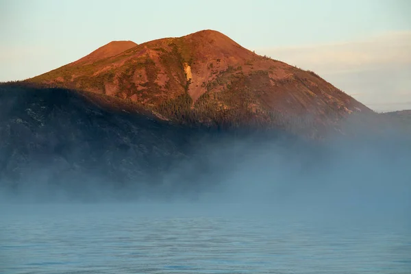 Mlha nad jezero a hory vrchol, v červené světlo. — Stock fotografie