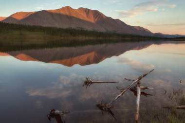 Dağın tepesinde düşük güneş ışığı. Göl dağlarda yansımasıdır. Yakutya.