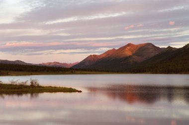 Dağın tepesinde düşük güneş ışığı. Göl dağlarda yansımasıdır. Yakutya.