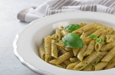 Açık mavi beyaz bir tabağa ev yapımı pesto soslu makarna