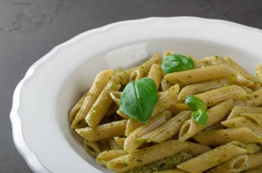 Karanlık bir taş üzerinde beyaz bir tabak içinde ev yapımı pesto soslu makarna