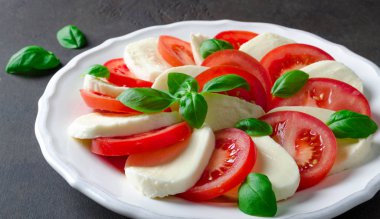 Beyaz bir tabağa dilimlenmiş domates ve mozzarella peyniri, karanlık taş geri