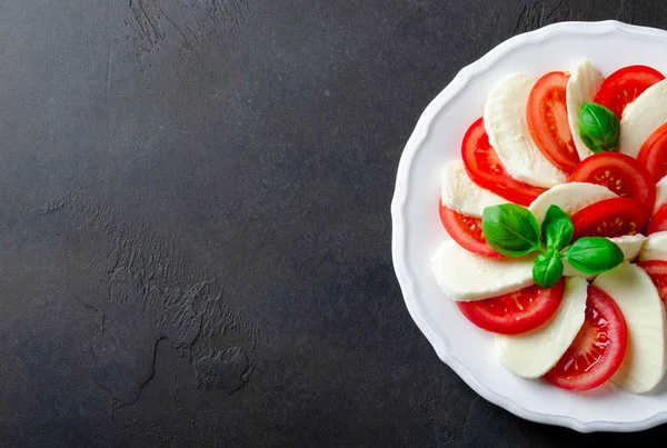Порезанные помидоры и моцарелла на белой тарелке, темный камень на спине — стоковое фото