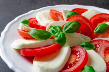 Beyaz bir tabağa dilimlenmiş domates ve mozzarella peyniri, karanlık taş geri