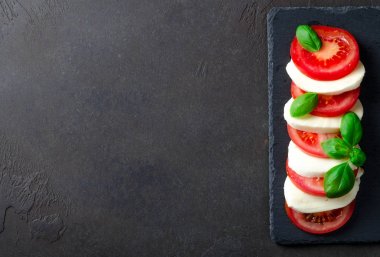 Kayrak bir tabağa dilimlenmiş domates ve mozzarella peyniri, karanlık taş geri