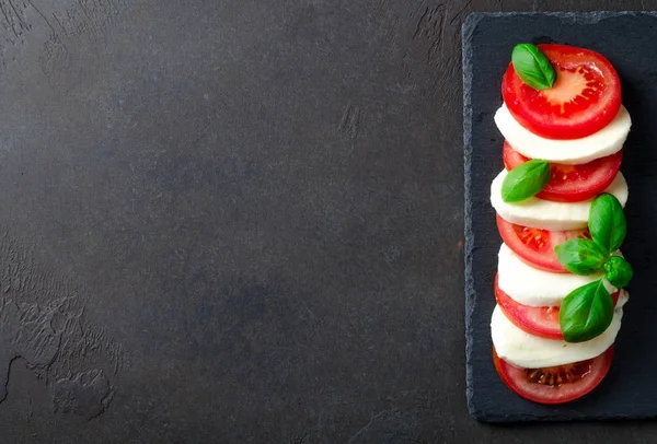 Нарезанные помидоры и моцарелла на тарелке, темный камень на спине — стоковое фото