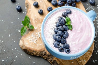 Böğürtlenli yoğurt ile karanlık bir taş tabloda clos rendelenmiş hindistan cevizi