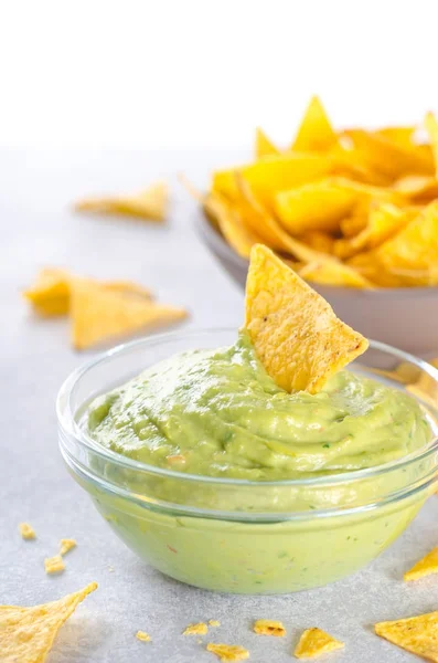 Tradizionale salsa di guacamole fatta in casa messicana in una ciotola di vetro e una ciotola con tortilla chips su uno sfondo di pietra chiara. Concetto di cibo da festa. Vista frontale, spazio di copia, immagine verticale, tasto alto — Foto Stock