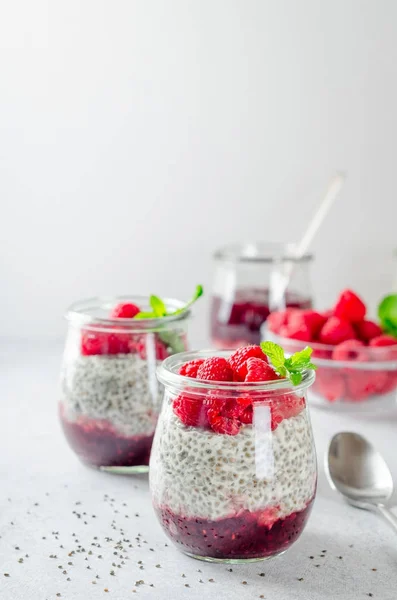 Due barattoli di vetro con pudding chia con lampone e marmellata. Ciotola di lampone sullo sfondo. Immagine verticale, spazio di copia, primo piano, vista frontale Immagine Stock