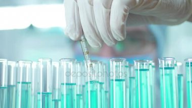 Bir laboratuarda, pipetli bir bilim adamı test tüplerindeki DNA ve molekülleri ayırmak için mavi bir sıvıyı analiz eder. Sıvıyla çalışan doktor..