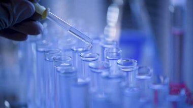 Bir laboratuarda, pipetli bir bilim adamı test tüplerindeki DNA ve molekülleri ayırmak için mavi bir sıvıyı analiz eder. Sıvıyla çalışan doktor..