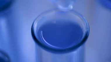 Bir laboratuarda, pipetli bir bilim adamı test tüplerindeki DNA ve molekülleri ayırmak için mavi bir sıvıyı analiz eder. Sıvıyla çalışan doktor..