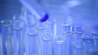 Bir laboratuarda, pipetli bir bilim adamı test tüplerindeki DNA ve molekülleri ayırmak için mavi bir sıvıyı analiz eder. Sıvıyla çalışan doktor..