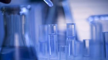 Bir laboratuarda, pipetli bir bilim adamı test tüplerindeki DNA ve molekülleri ayırmak için mavi bir sıvıyı analiz eder. Sıvıyla çalışan doktor..