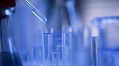 Bir laboratuarda, pipetli bir bilim adamı test tüplerindeki DNA ve molekülleri ayırmak için mavi bir sıvıyı analiz eder. Sıvıyla çalışan doktor..