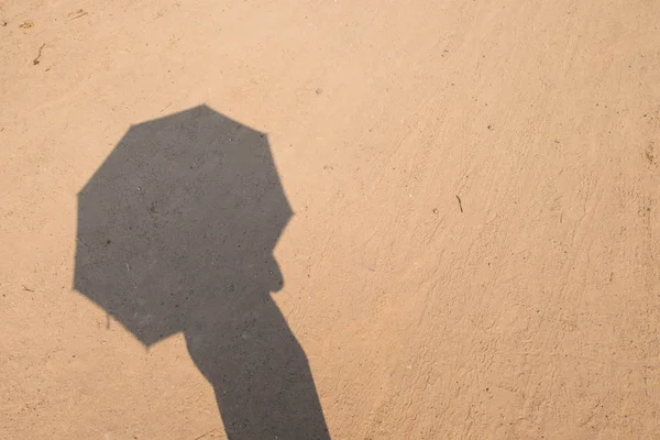 Ombre de quelqu'un avec parapluie sur le sol de sable avec des pistes de roue Photo De Stock