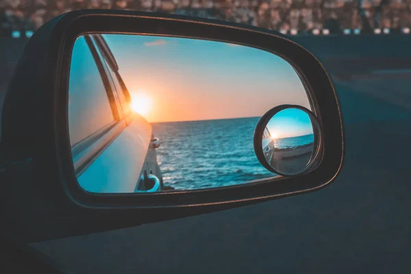 Reflection of the beautiful sunset above the sea through the car\'s wing mirror in the parking lot close to the sea