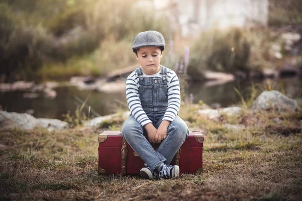 Criança triste sentada em uma mala — Fotografia de Stock